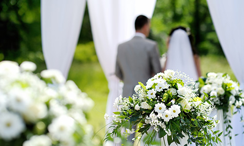 A bride and groom stand, surrounded by delicate white flowers and white fabric.
