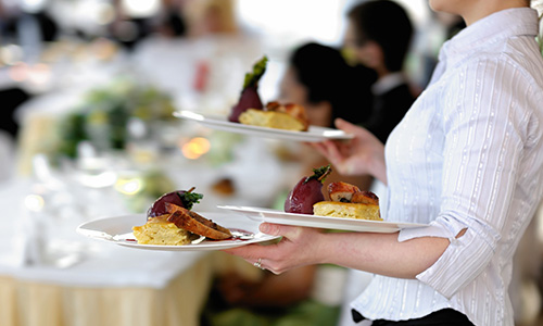 A server carries plates of gourmet food to tables.