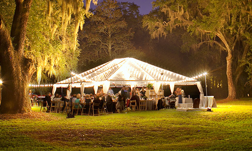 Simple white tent in a field lit up beautifully at night with white lights.