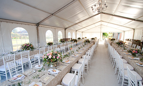 A long tent filled with elegantly set banquet tables on sophisticated hard flooring.