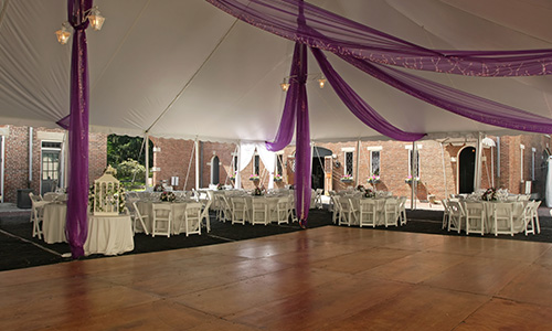 This large dance floor is laid with wood flooring and accented with white tables and purple decorations.