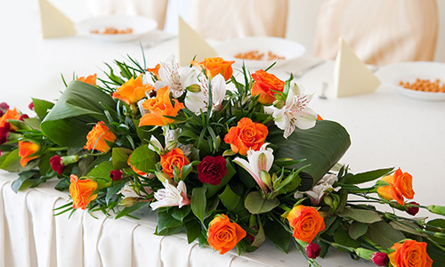 A floral centerpiece decorates a table in white, orange, and red, with foliage.