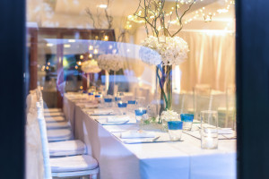 A long rectangle table set with blue decorations and white flowers.