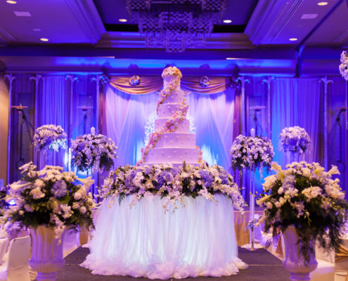 Indoor wedding reception, multi-tier white cake with floral arrangements and blue lighting.