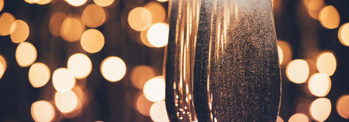 Two bubbling champagne glasses are pictured, while blurry lights in the background imply a festive setting.