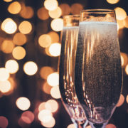 Two bubbling champagne glasses are pictured, while blurry lights in the background imply a festive setting.