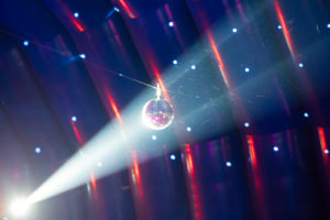 A light shines on a disco ball, with even more party lights present in the background.